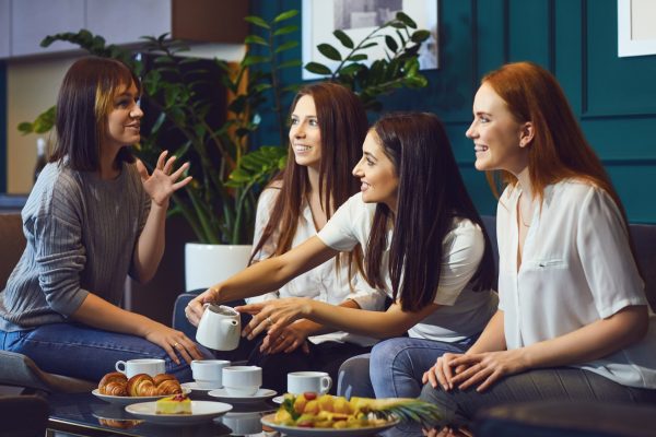 Charming casual women sitting on sofa in modern interior having tea and chatting